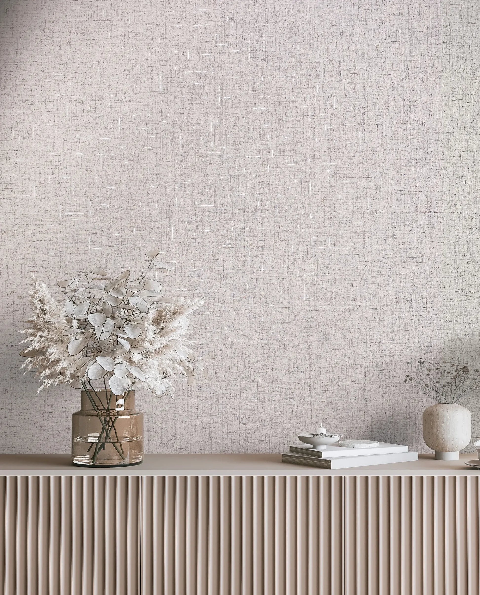 Marburg City Romance 35113 Light beige and gray crosshatch wallpaper behind a fluted console styled with a glass vase of dried leaves, a small ceramic vase with stems, stacked books, and a shallow dish.