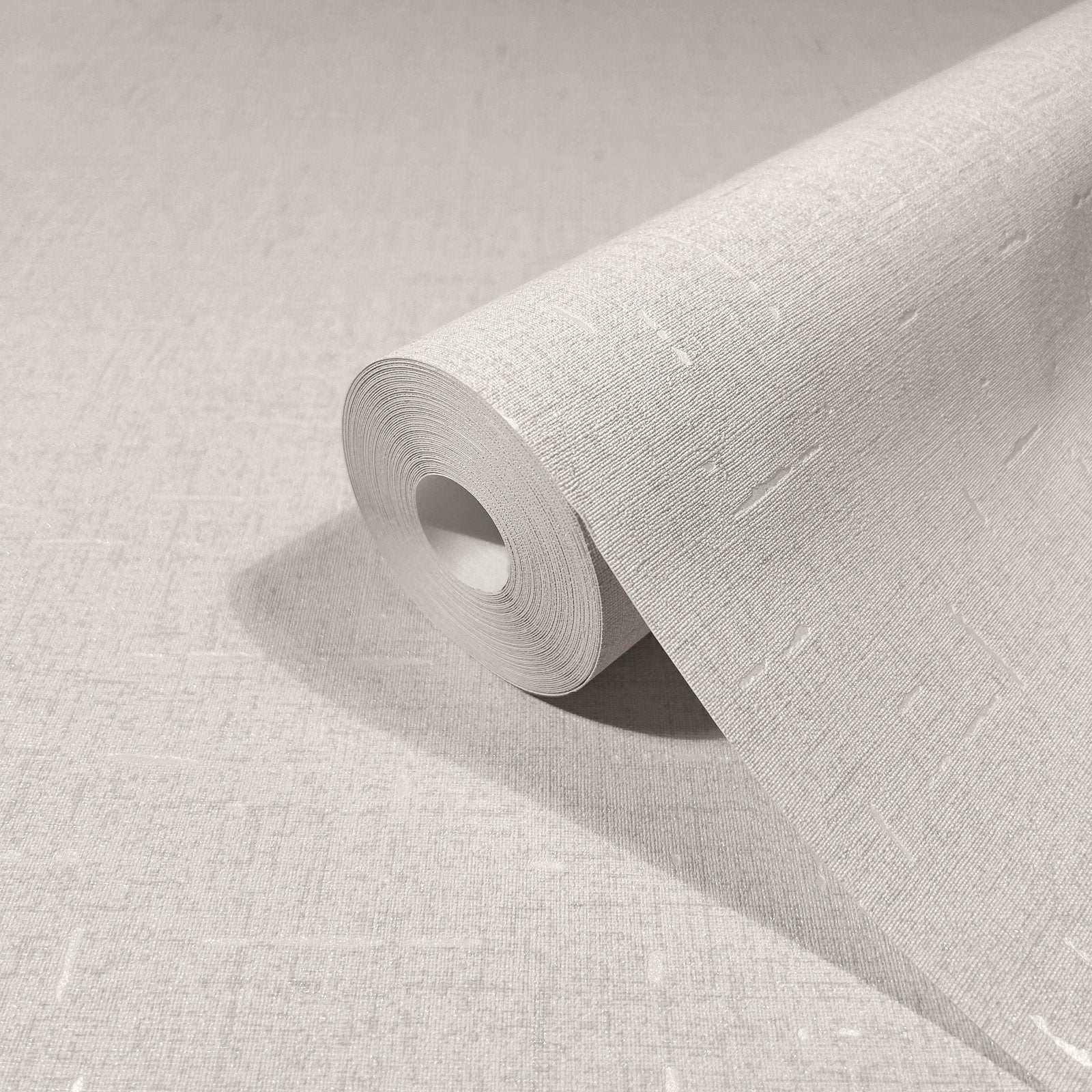 Marburg City Romance 35114 Angled roll of beige textured wallpaper with a fine linen-like weave and subtle light slubs, resting on matching unrolled wallpaper.