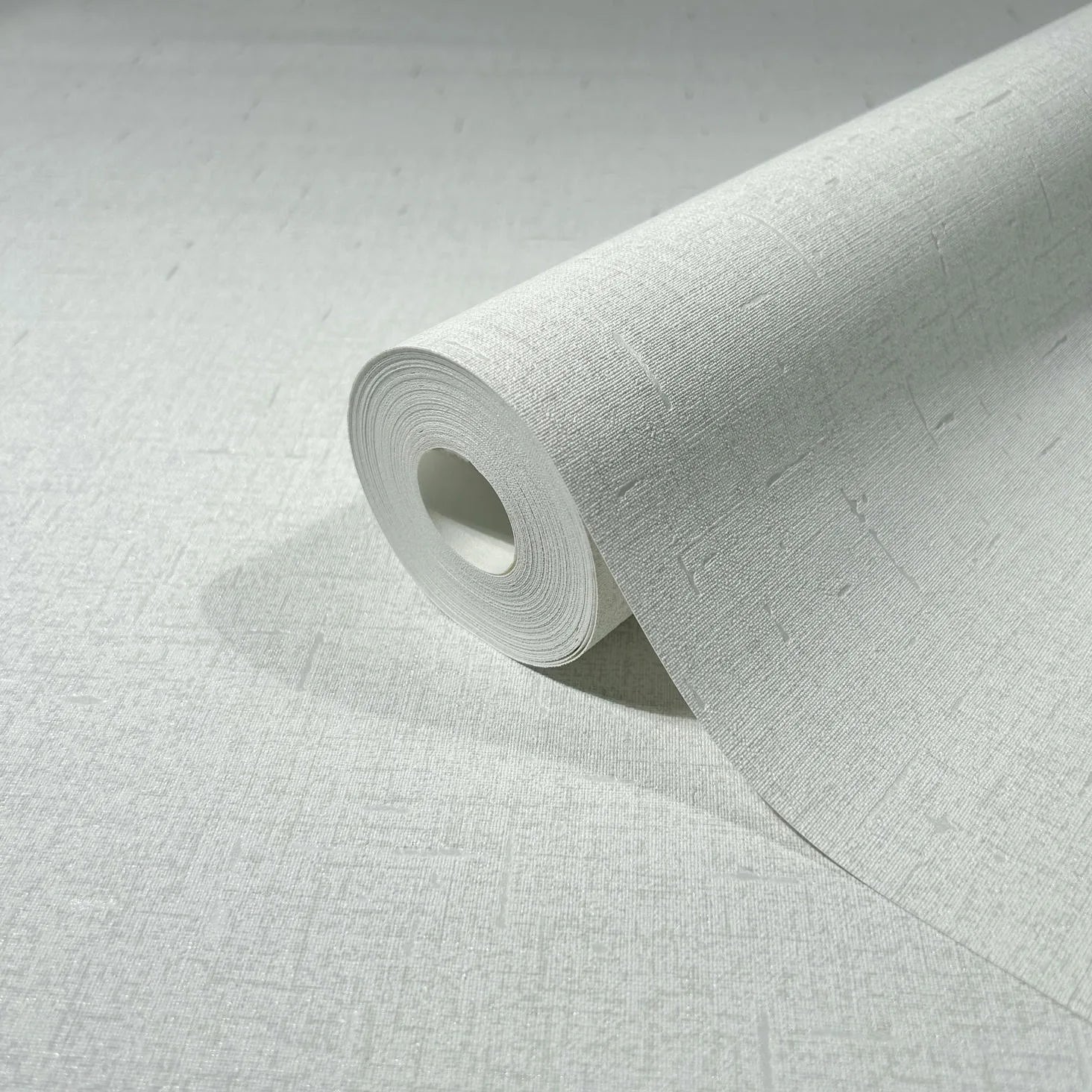 Marburg City Romance 35115 A close-up of a wallpaper roll partially unrolled on a matching light textured surface, showing a subtle crosshatch with small linear dash details.