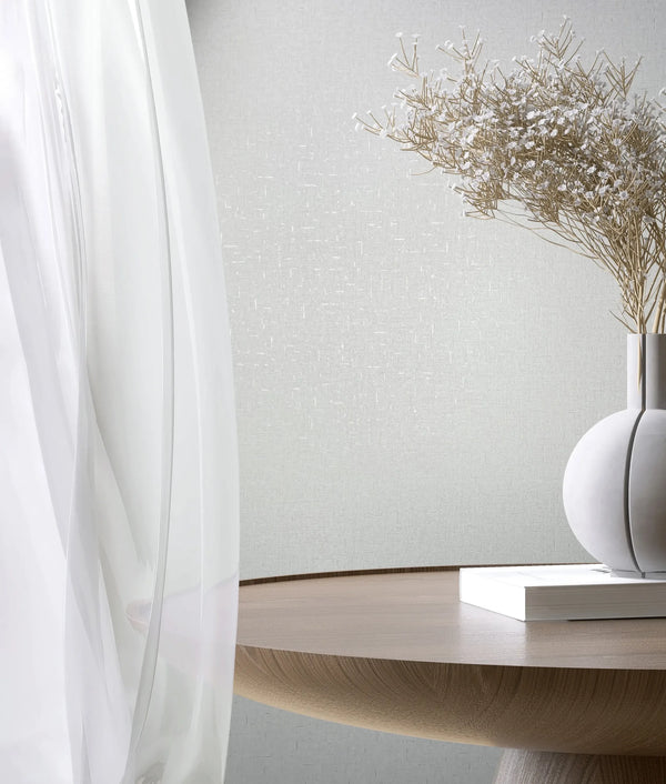 Marburg City Romance 35115 White textured wallpaper with a subtle crosshatch look behind a sheer curtain, a round wooden table, a spherical vase holding dried stems, and a closed book.