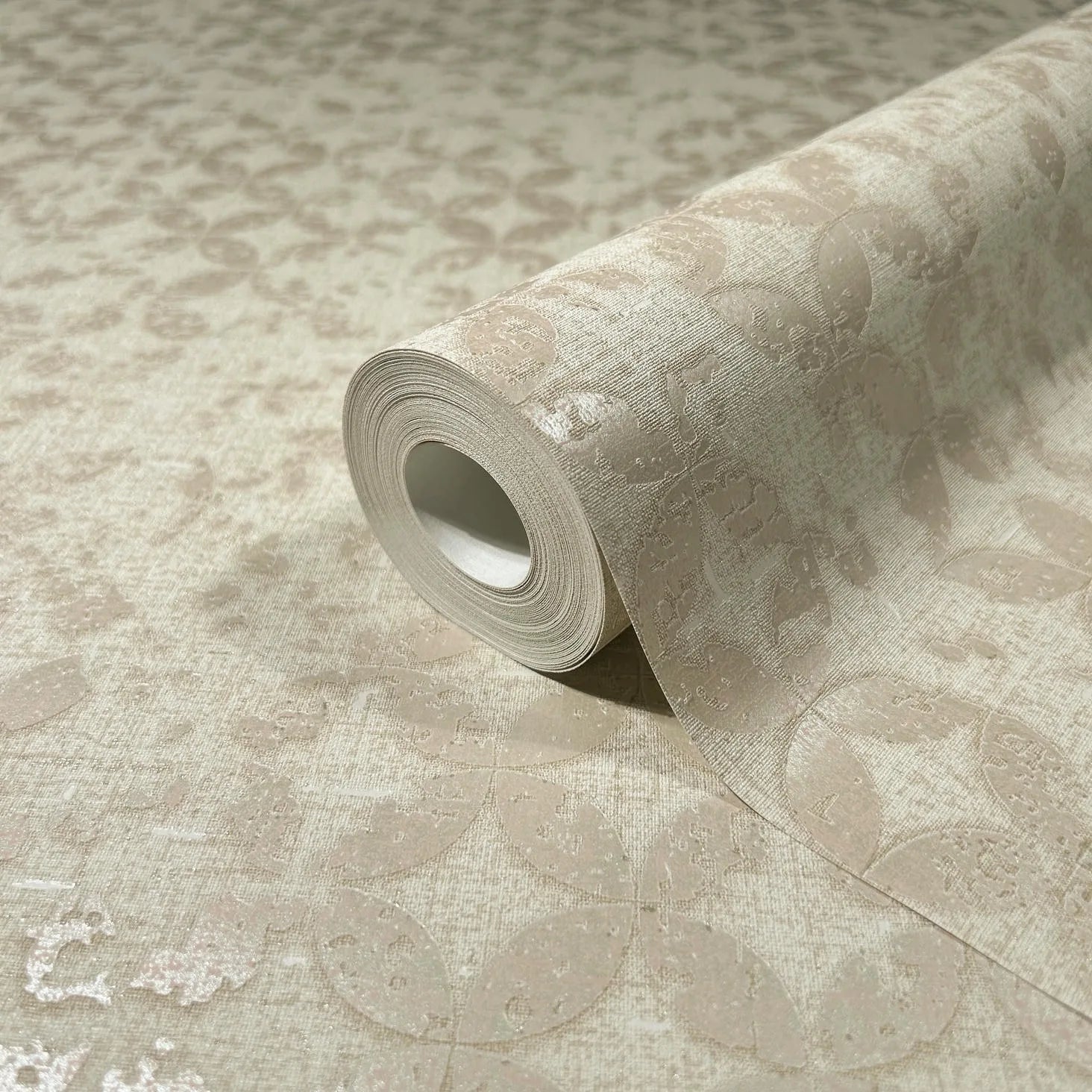 Marburg City Romance 35117 A beige wallpaper roll resting on a matching unrolled sheet, showing a subtle tonal oval or leaf pattern with a slight sheen.