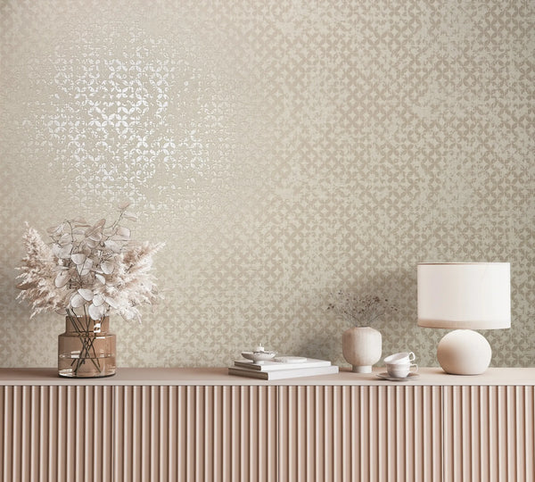 Marburg City Romance 35117 Beige wallpaper with a small repeating lattice pattern and a soft sheen shown behind a ribbed sideboard topped with a glass vase of dried stems, a round-base table lamp, a small ceramic vase, stacked books, and a cup with saucer.