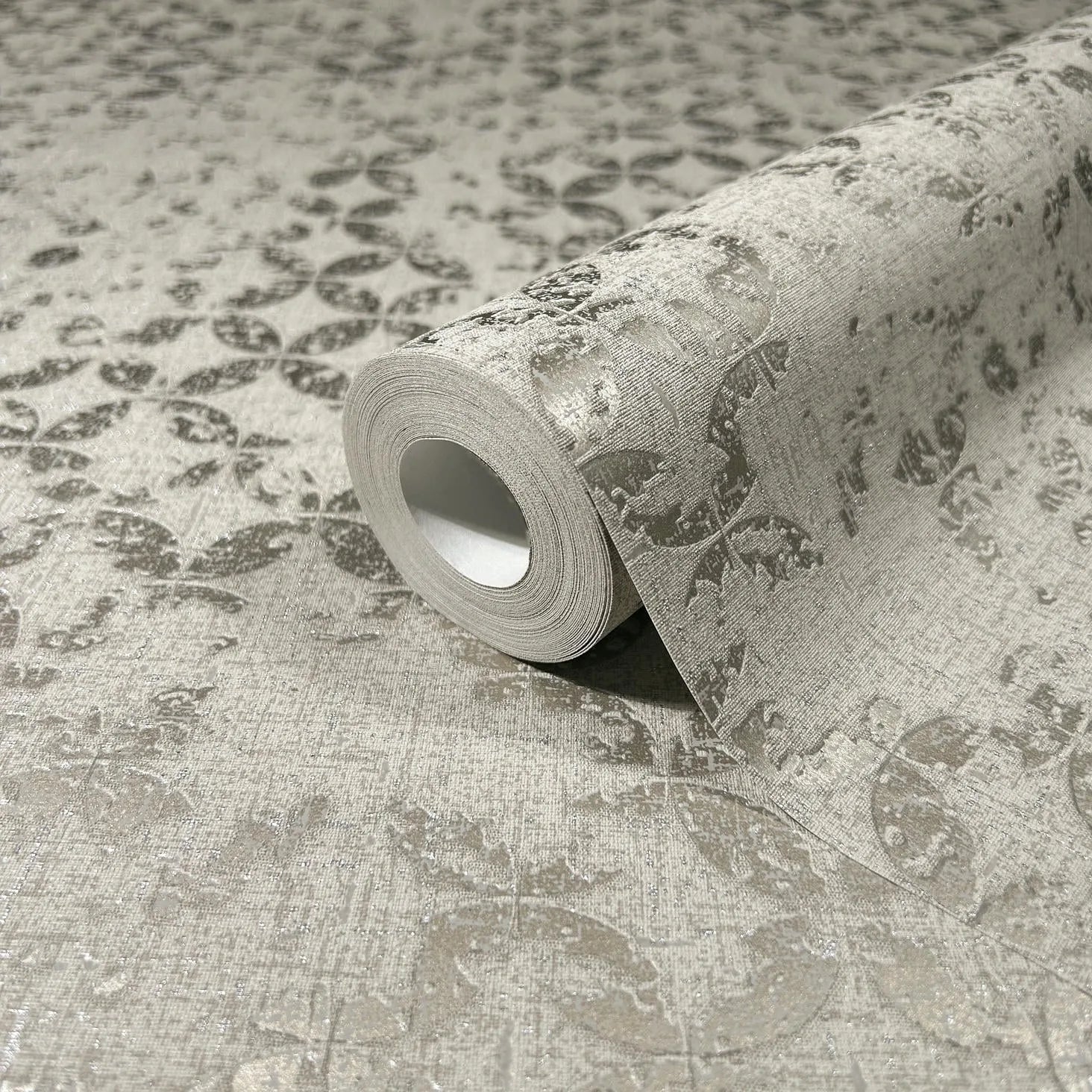 Marburg City Romance 35118 Close-up of a gray wallpaper roll on a matching surface, showing a repeating leaf-and-circle motif on a textured background.