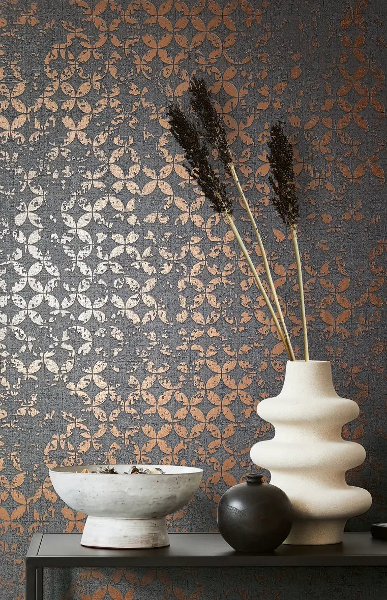Marburg City Romance 35119 Dark charcoal wallpaper with a distressed metallic circular motif, styled with a cream sculptural vase holding tall dried stems, a small black round vase, and a white footed bowl on a narrow shelf.