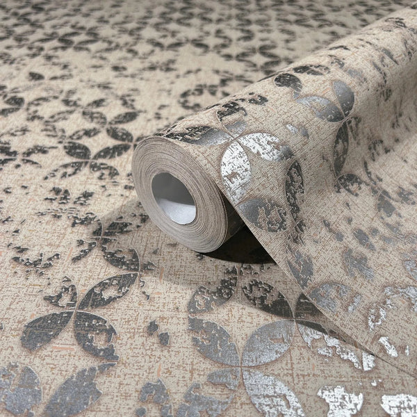 Marburg City Romance 35120 Close-up of a wallpaper roll resting on matching beige wallpaper, showing a repeating metallic gray petal motif and textured surface.
