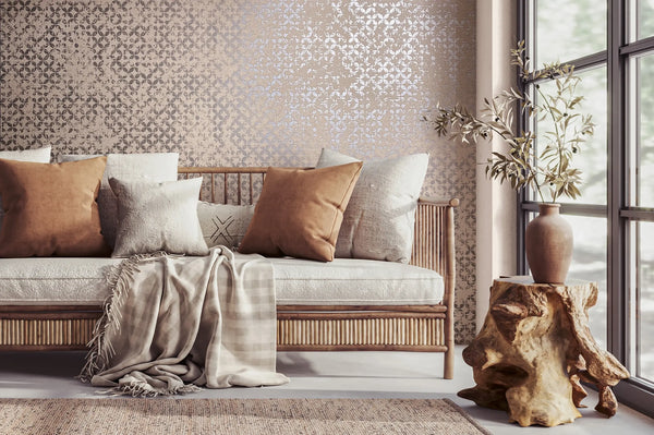 Marburg City Romance 35120 Beige wallpaper with a small repeating damask-style pattern behind a rattan sofa with neutral pillows and a draped throw, next to a stump side table holding a vase with branches by a large window.