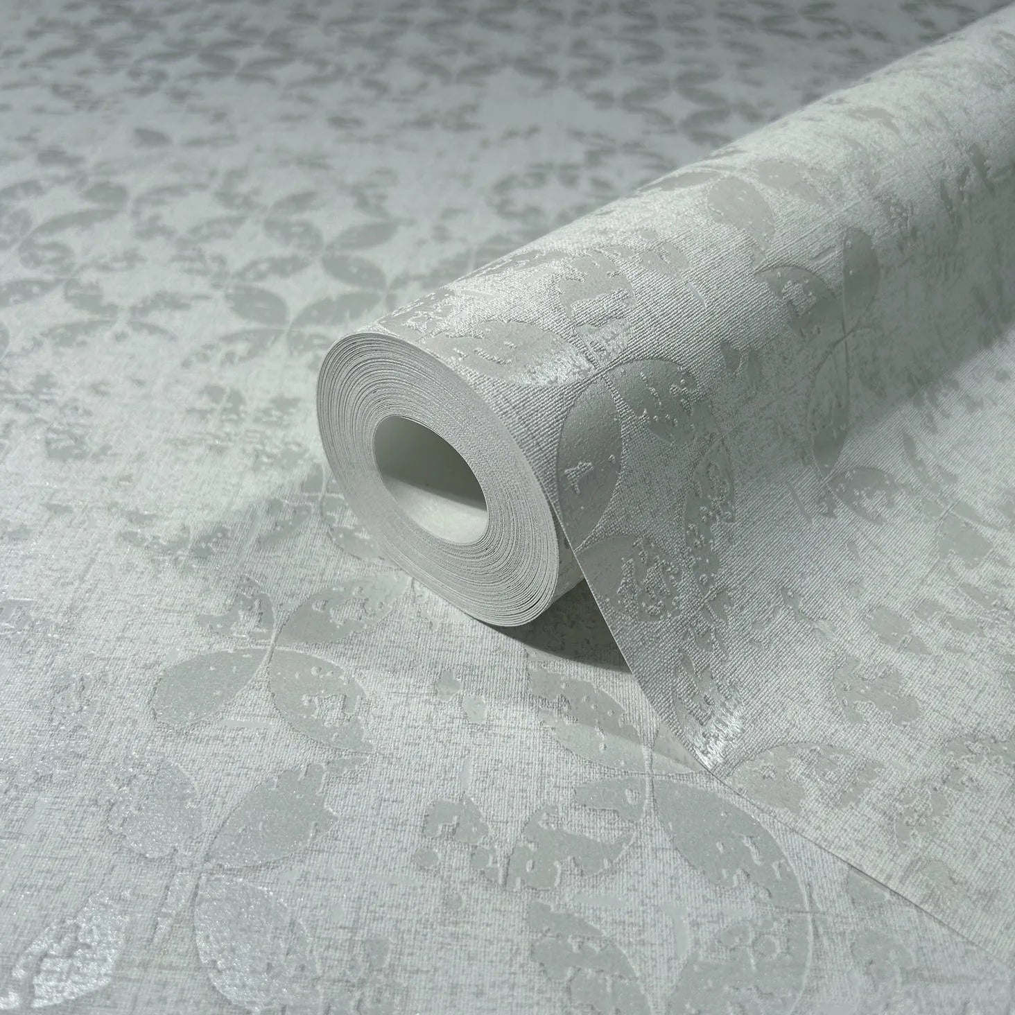 Marburg City Romance 35121 Close-up of a wallpaper roll on matching surface showing a light grey tonal leaf pattern with subtle texture.