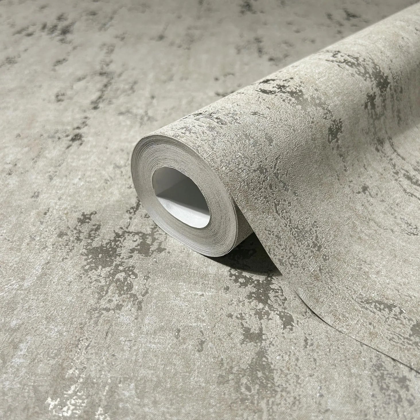 Marburg City Romance 35123 Close-up of a gray wallpaper roll with an abstract mottled texture resting on a matching unrolled section.