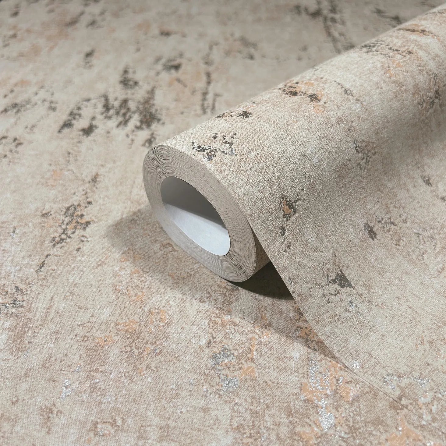 Marburg City Romance 35124 Close-up of a beige mottled, distressed-effect wallpaper shown as a partially unrolled roll on the same surface.