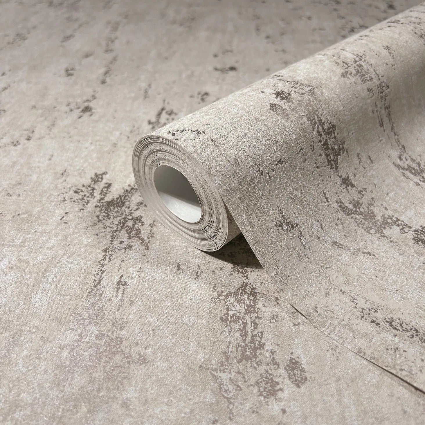 Marburg City Romance 35125 Close-up of a beige wallpaper roll with a mottled, distressed texture, resting on the same pattern.