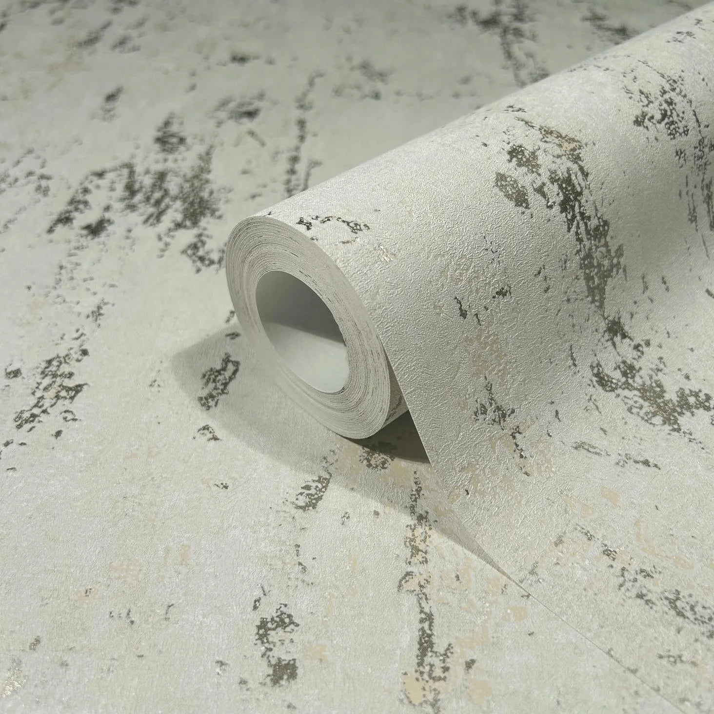 Marburg City Romance 35127 Close-up of a wallpaper roll resting on the same paper, showing a light beige ground with irregular gray mottled streaks and a textured surface.