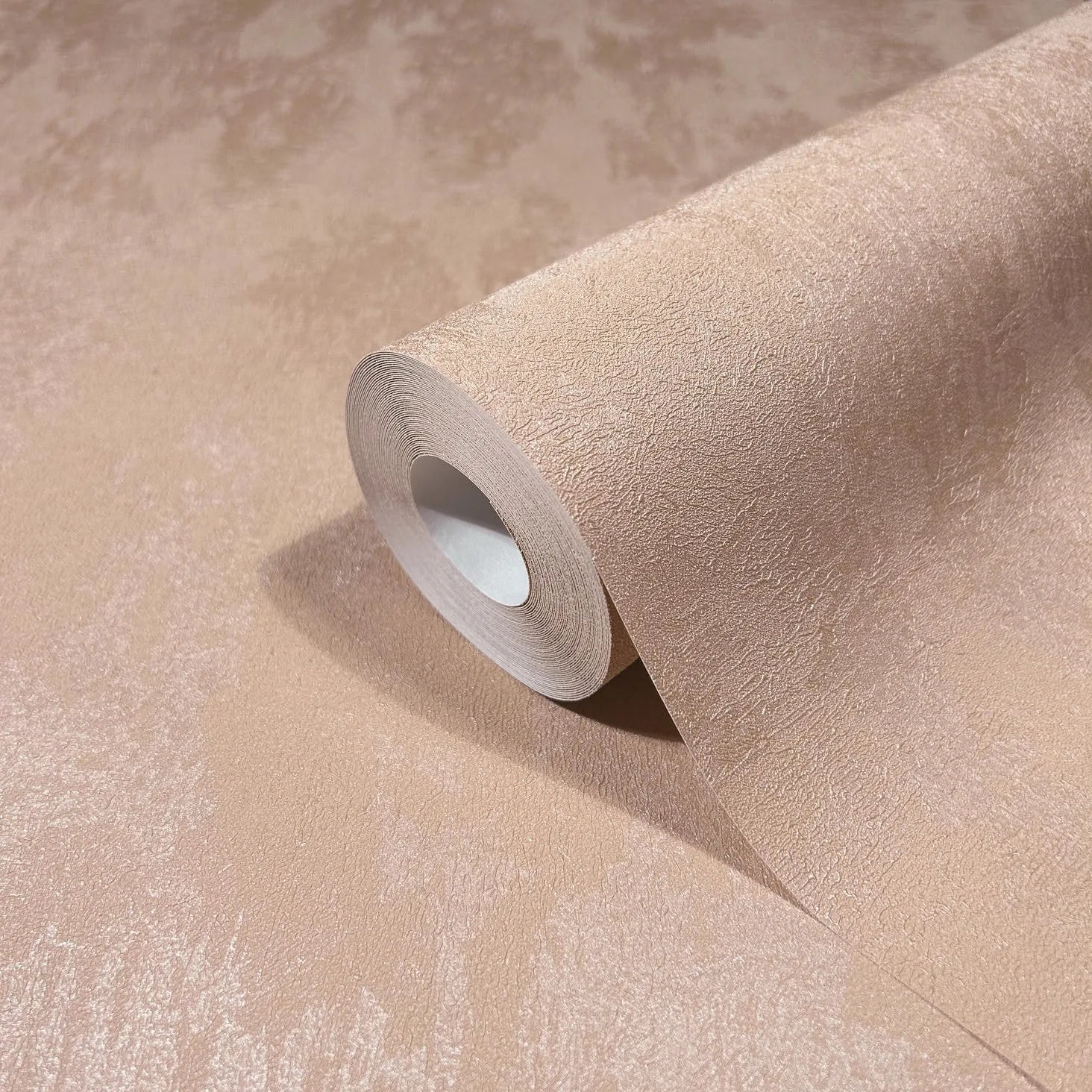 Marburg City Romance 35129 Close-up of a wallpaper roll partially unrolled on a matching sheet, showing a warm peach tone-on-tone textured, lightly mottled finish.