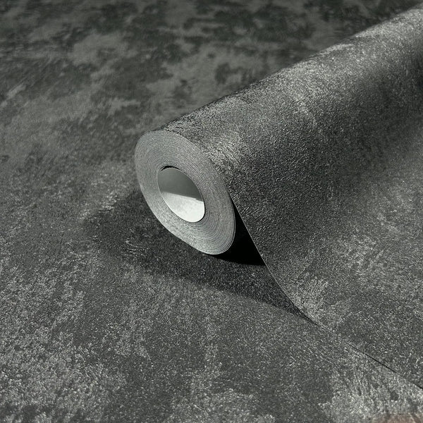 Marburg City Romance 35130 Close-up of a partially unrolled wallpaper roll resting on the same dark gray mottled textured wallpaper, showing a subtle sheen.