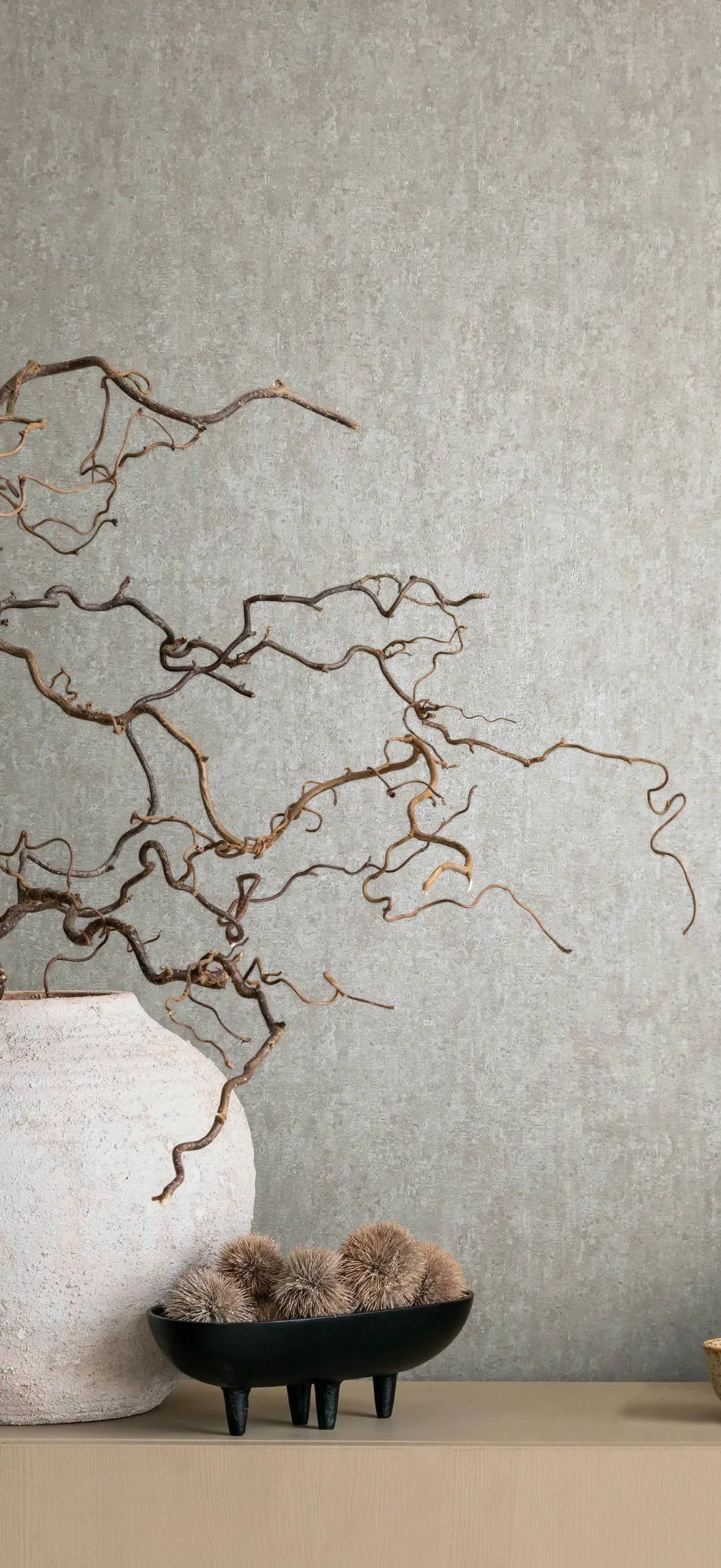 Marburg 35134 wallpaper lounge feature wall with a simple console, large ceramic vase of twisting branches and a black footed bowl of dried pods, calm and natural.