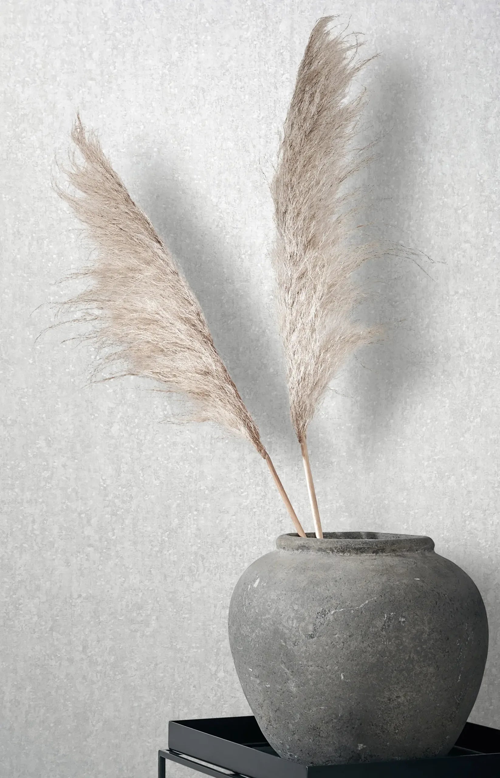 Marburg 35135 wallpaper lounge feature wall with subtle textured finish behind a stone vase holding two pampas stems on a black metal side table, calm minimalist mood.