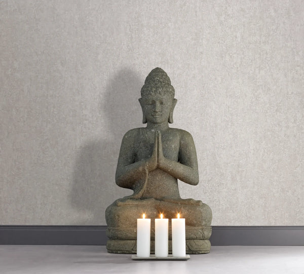 Marburg 35136 wallpaper lounge feature wall with textured surface, stone Buddha statue and four lit pillar candles on the floor, serene and minimalist.