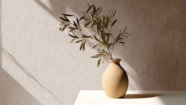Marburg 35138 wallpaper lounge feature wall behind a sunlit side table with a ceramic vase and leafy branch, calm minimalist mood.
