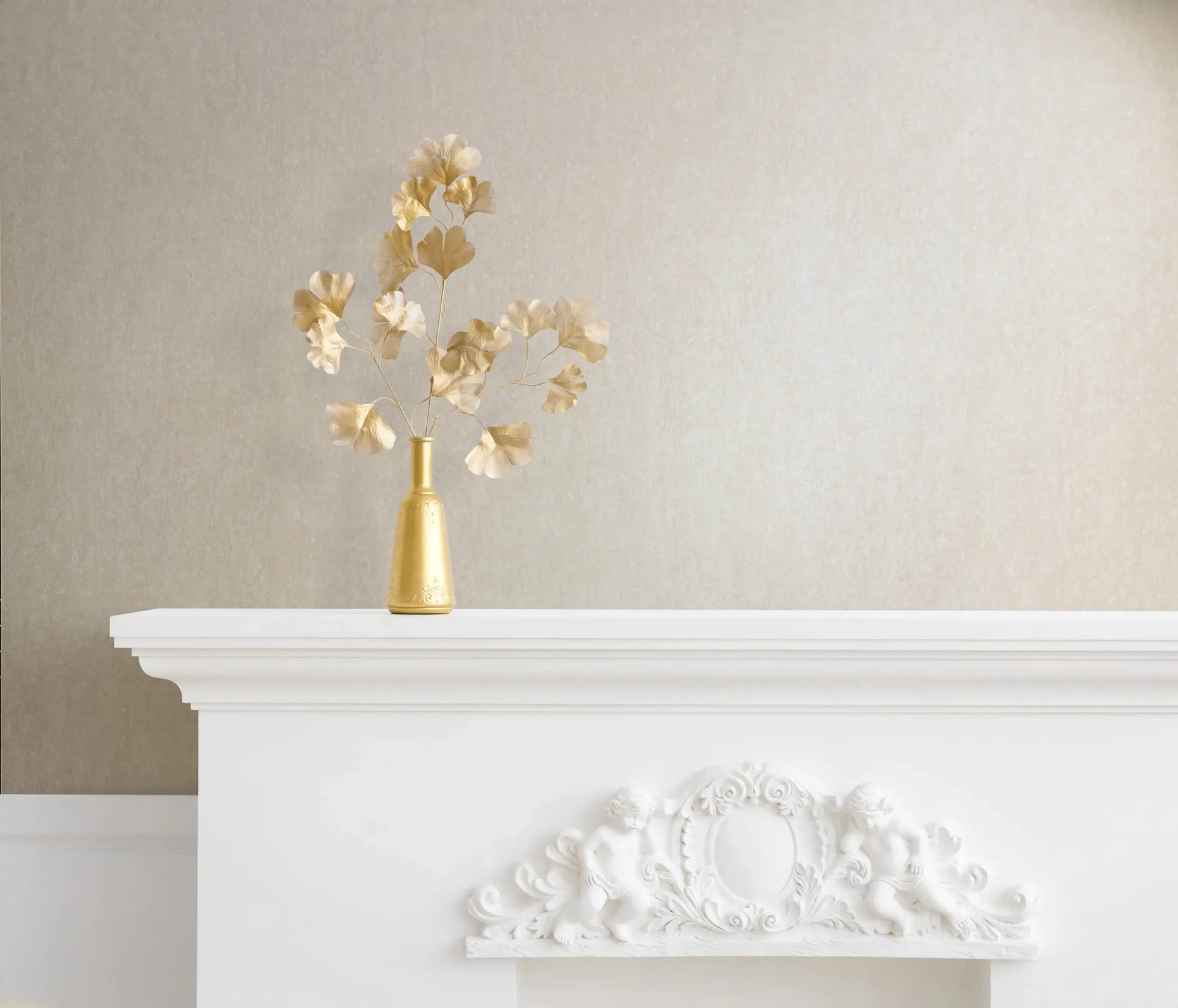 Marburg 35139 wallpaper lounge feature wall behind an ornate white mantel with cherub relief and a gold vase of metal leaves, calm and elegant.