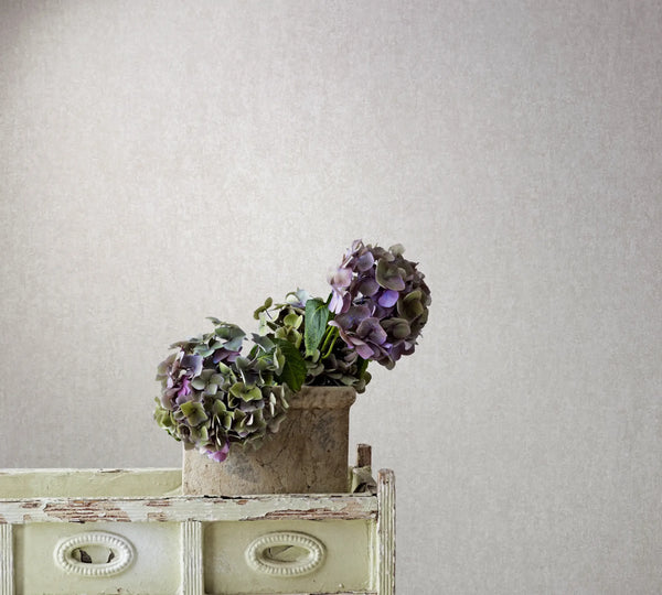 Marburg 35140 wallpaper lounge feature wall behind a distressed sideboard topped with a rustic stone pot of hydrangeas, calm vintage vibe.