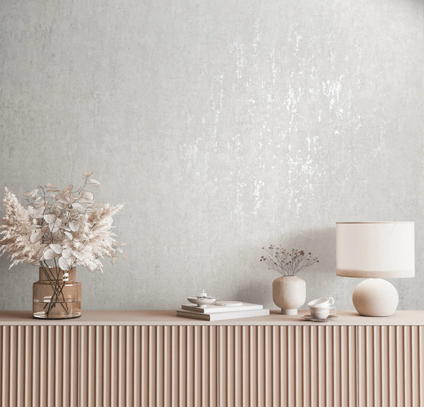 Marburg 35143 wallpaper lounge feature wall behind a fluted sideboard with a glass vase of dried foliage, books, cups and a round table lamp, creating a calm minimalist mood.