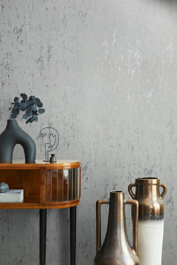 Marburg 35144 wallpaper lounge feature wall with distressed texture behind a wood console and sculptural vase, beside tall metallic vases for a calm modern look.