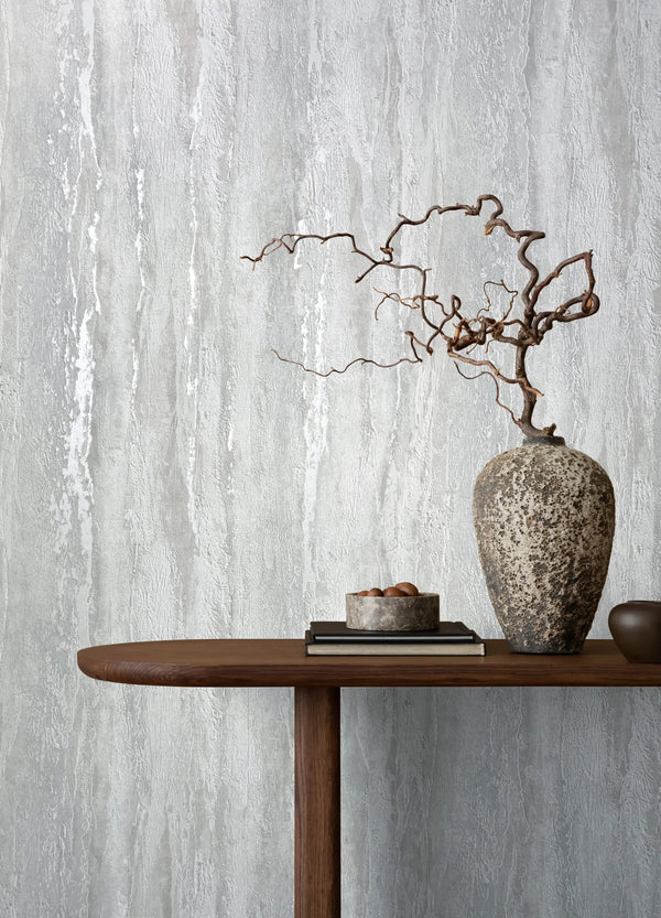 Marburg 35155 wallpaper lounge feature wall with textured vertical finish, wooden console table, rustic stone vase with bare branches, books and small bowl, serene mood.