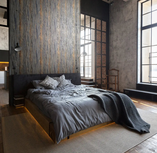 Marburg 35156 wallpaper in an industrial loft bedroom with a textured feature wall behind a low platform bed, black-framed grid windows, exposed brick accents, metal task lamps, and a moody cozy feel.
