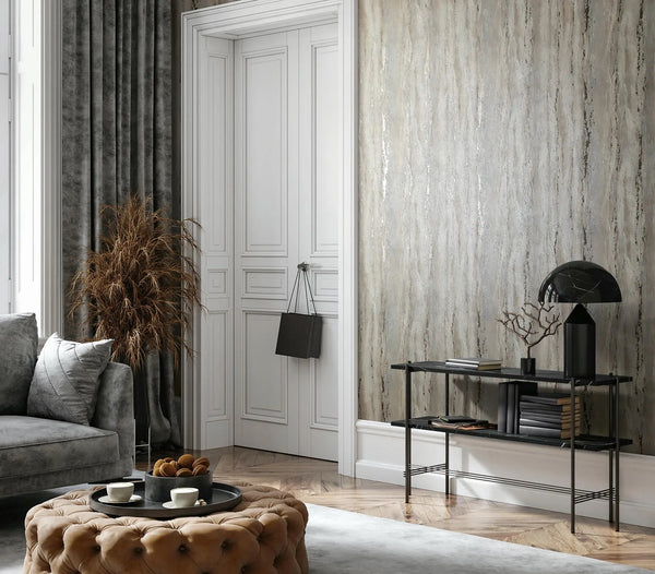 Marburg 35159 wallpaper lounge feature wall with textured finish beside a paneled door, black console with sculptural lamp and books, grey sofa and tufted ottoman with tray, dried grass and heavy drapes, calm modern mood.