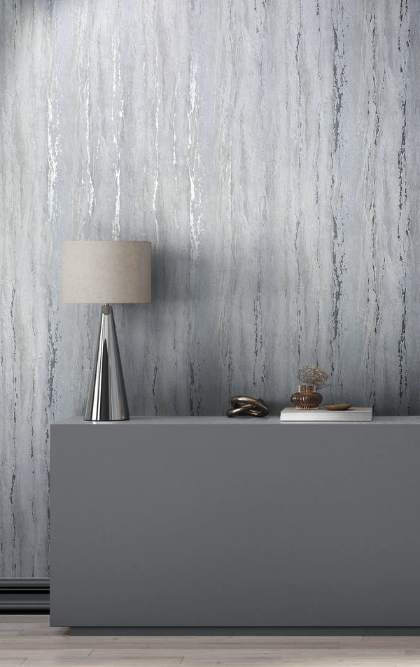 Marburg 35160 wallpaper lounge feature wall with textured grey vertical pattern behind a grey console holding a metallic cone lamp, sculptural knot, glass vase on a book, and small dish for a calm minimalist mood.
