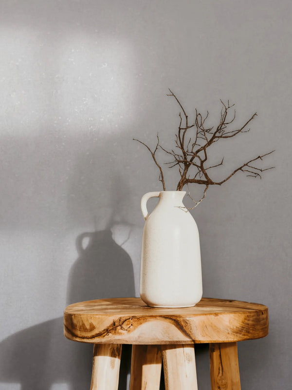 Marburg 35161 wallpaper lounge feature wall behind a rustic wooden stool topped with a ceramic jug and dried branches, minimalist and serene.