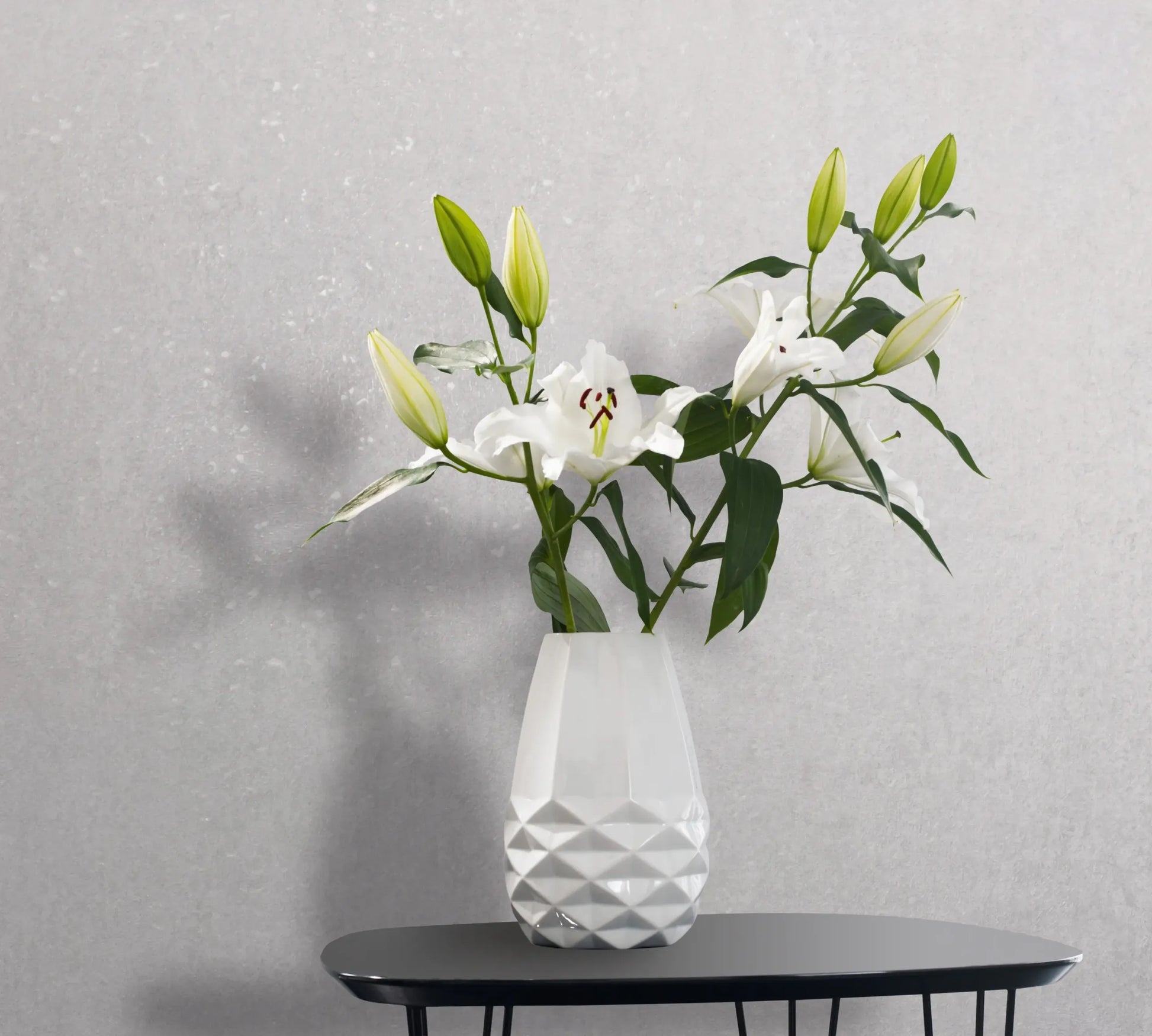 Marburg 35161 wallpaper in a lounge feature wall behind a black side table holding a white faceted vase of white lilies for a calm minimalist look.