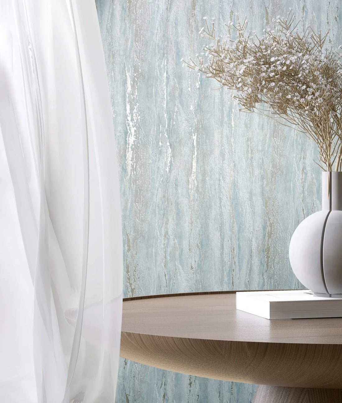 Marburg 35165 wallpaper lounge feature wall with softly textured finish, round wooden table, sculptural vase of dried stems and a book beside a sheer curtain, calm and airy.