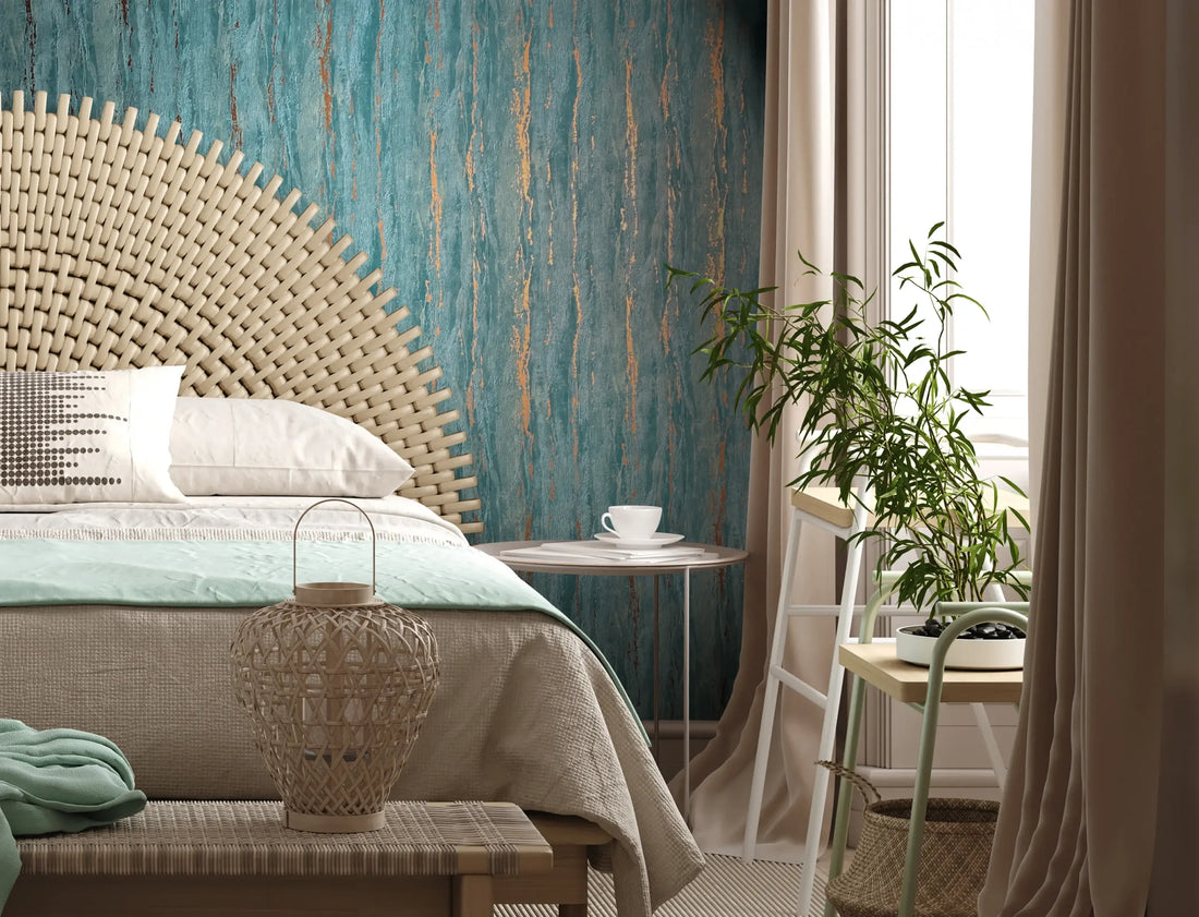 Marburg 35167 wallpaper in a serene bedroom feature wall behind a woven headboard, with small side table and cup, potted plant, wicker lantern on a bench, and soft curtains.