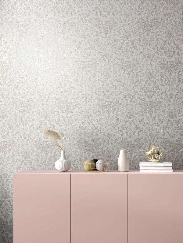 Marburg 35168 wallpaper lounge feature wall with ornate damask pattern behind a pale pink sideboard styled with white vases, a gold wire basket, stacked books, and a geometric ornament, calm and elegant.
