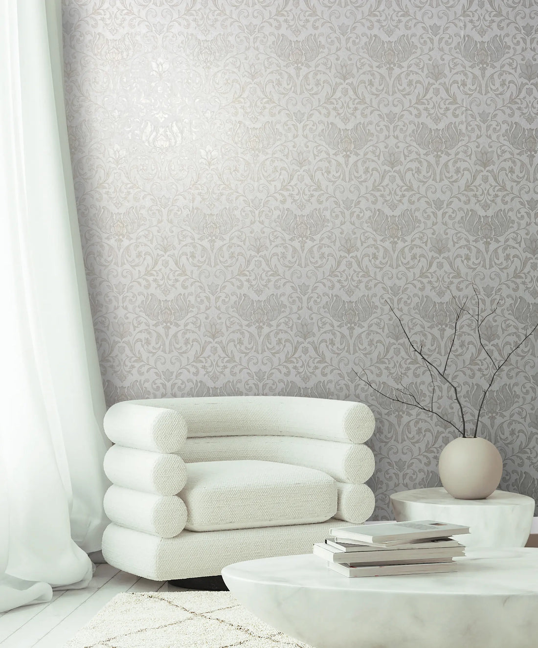 Marburg 35168 wallpaper lounge feature wall with damask pattern, sculptural white armchair, low stone tables with books, round vase with bare branches, airy and calm.