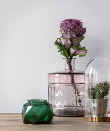 Marburg 47603 wallpaper in a lounge feature wall behind a wooden console with a pink glass vase and purple flower, green glass jar, and a cactus under a glass cloche, calm modern feel.