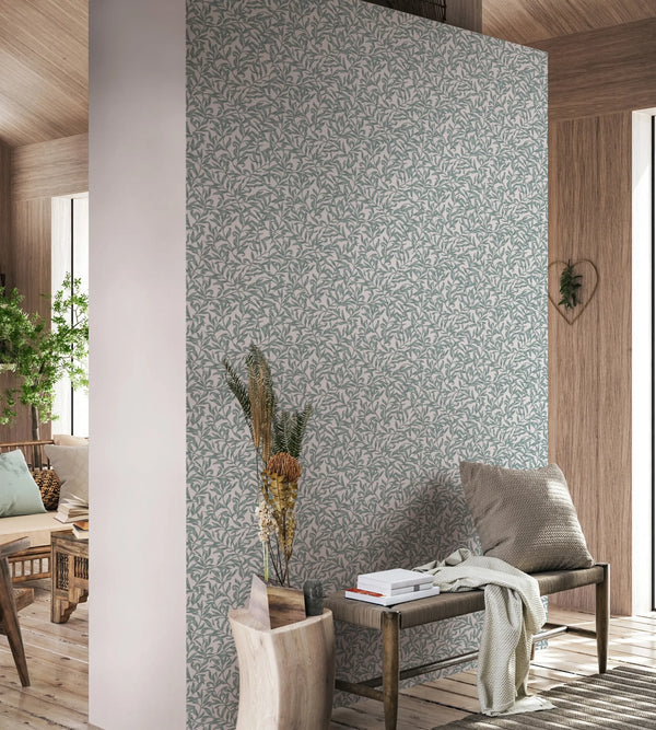 Marburg 47603 wallpaper in a serene lounge with a leafy feature wall, bench with cushion and throw, stacked books, dried botanicals, and natural wood accents.