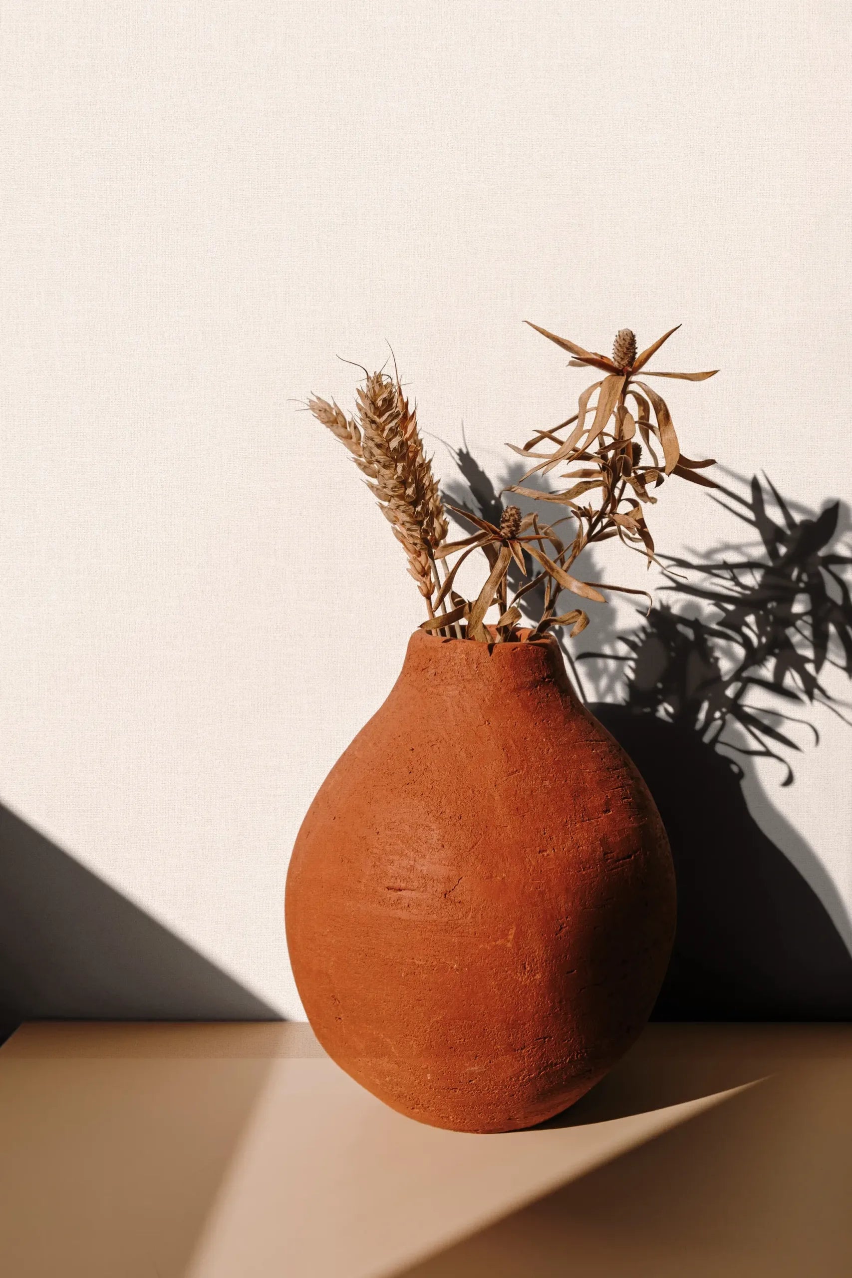 Marburg 47607 wallpaper lounge feature wall with a shelf and terracotta vase of dried stems casting soft shadows.