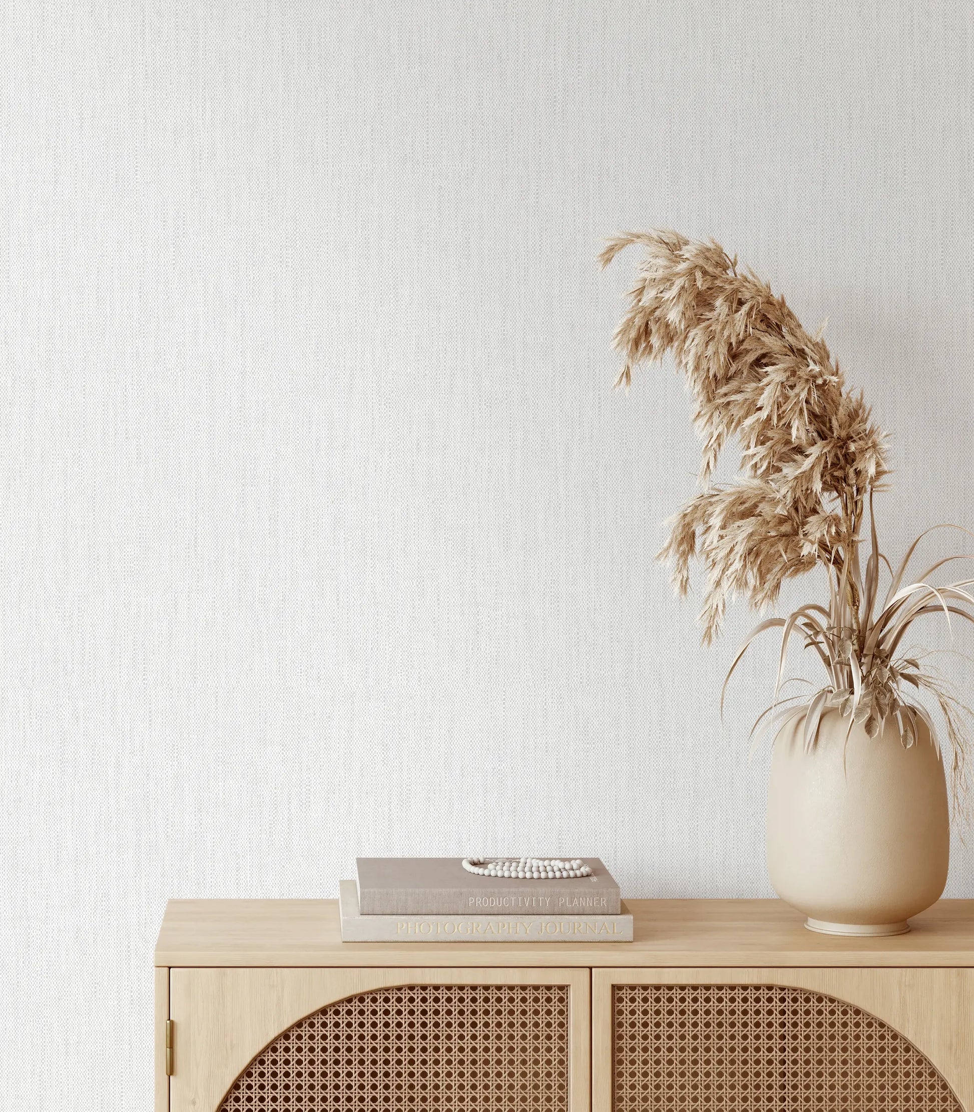 Marburg 47611 wallpaper lounge feature wall behind a light wood rattan sideboard with stacked books and a ceramic vase of dried grasses, minimal and serene.