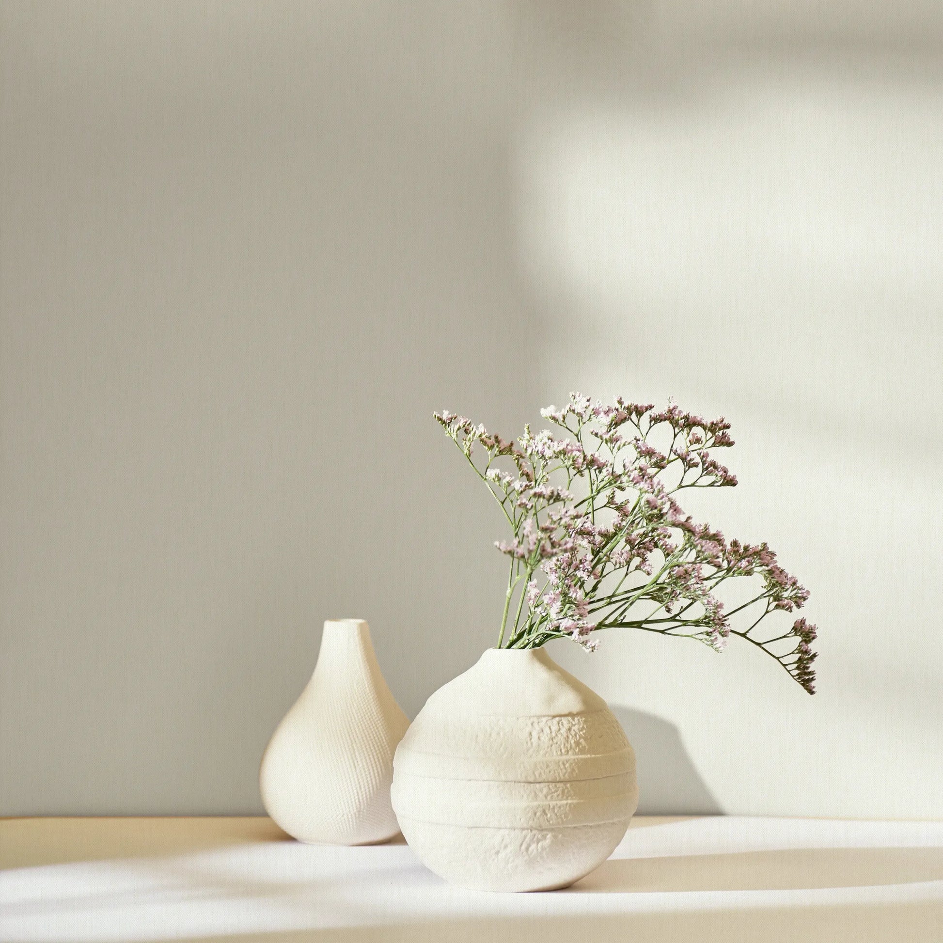 Marburg 47612 wallpaper lounge feature wall with a tabletop holding ceramic vases and delicate flowers in soft sunlight, calm minimalist mood.