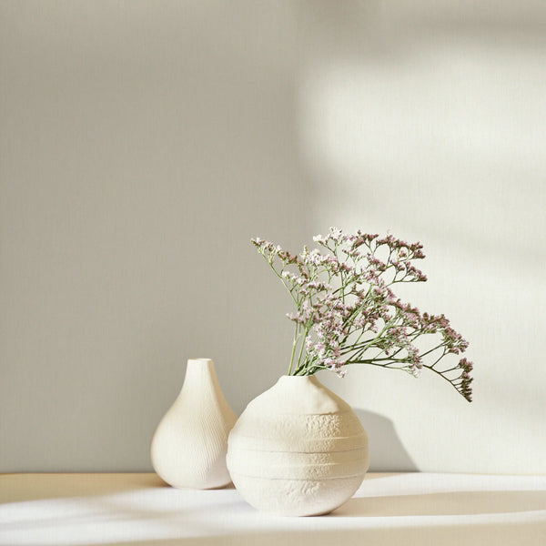 Marburg 47612 wallpaper lounge feature wall with a tabletop holding ceramic vases and delicate flowers in soft sunlight, calm minimalist mood.