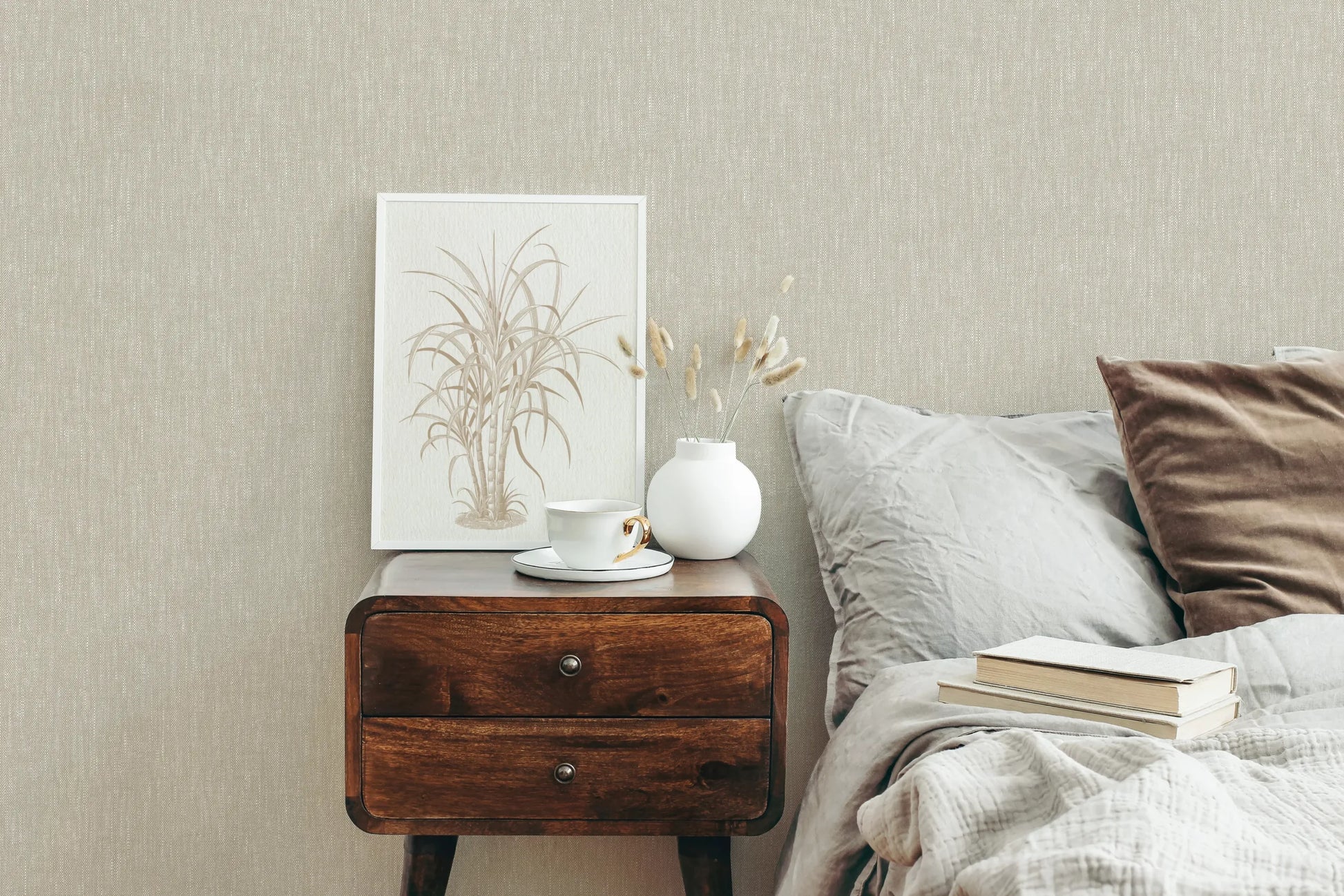 Marburg 47613 wallpaper bedroom feature wall behind a wooden bedside table with framed botanical art, white vase and teacup, beside a bed with pillows and books for a calm cozy mood.
