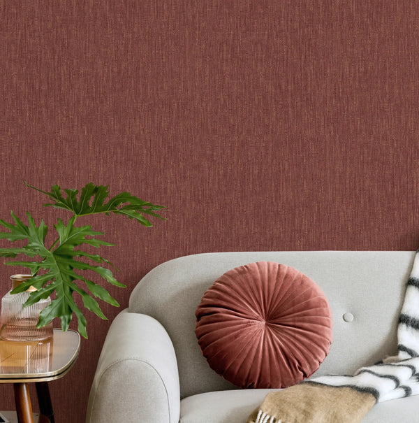 Marburg 47617 wallpaper lounge feature wall behind a light sofa with a round velvet cushion, striped throw, and a side table with a leafy plant, cozy modern vibe.