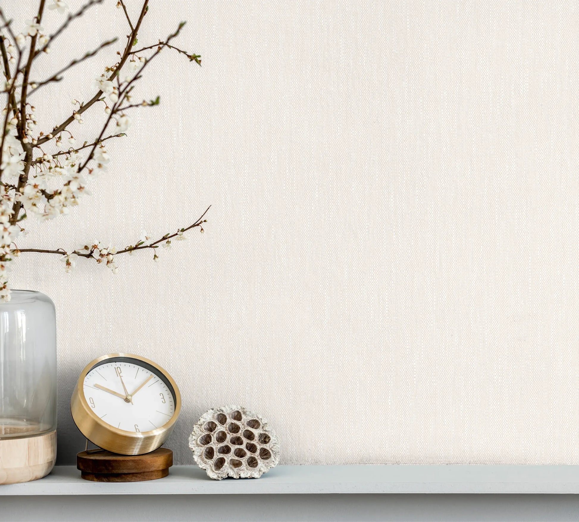 Marburg 47618 wallpaper lounge feature wall behind a slim shelf with a glass vase of blossom branches, a small clock and a natural decorative pod, calm minimalist mood.