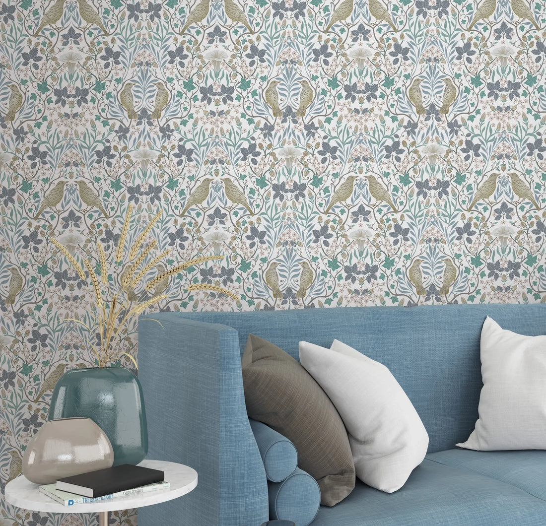 Marburg 47619 wallpaper lounge feature wall with ornate botanical pattern behind a blue sofa, mixed cushions, and a small side table with ceramic vases and dried grasses for a calm, cozy feel.