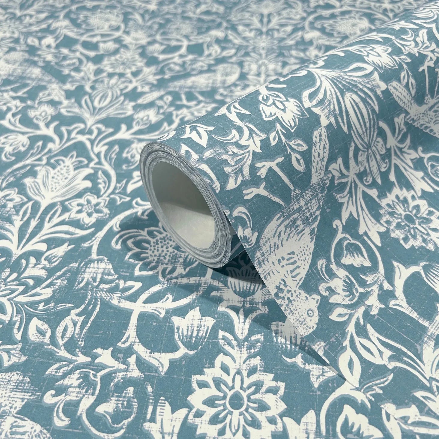 Marburg 47623 wallpaper roll close-up with white floral and bird pattern on blue background.