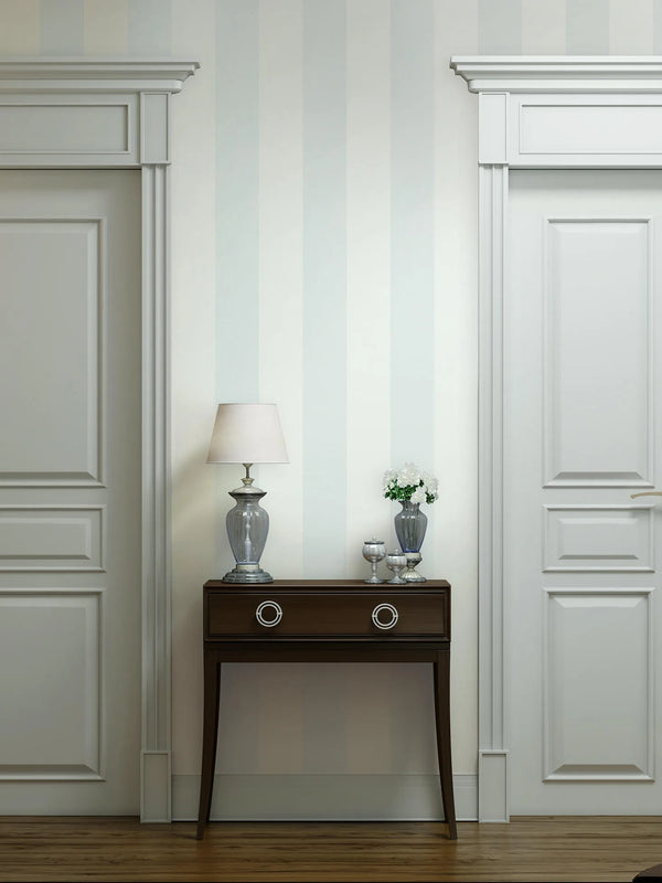 Marburg 47635 wallpaper lounge feature wall with soft vertical stripes, dark wood console between paneled doors, glass lamp and vase of white flowers, calm classic feel.