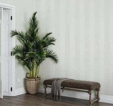 Marburg 47637 wallpaper lounge feature wall with subtle vertical stripes, a tall palm in a woven basket and an upholstered bench with a draped throw, relaxed and minimal.