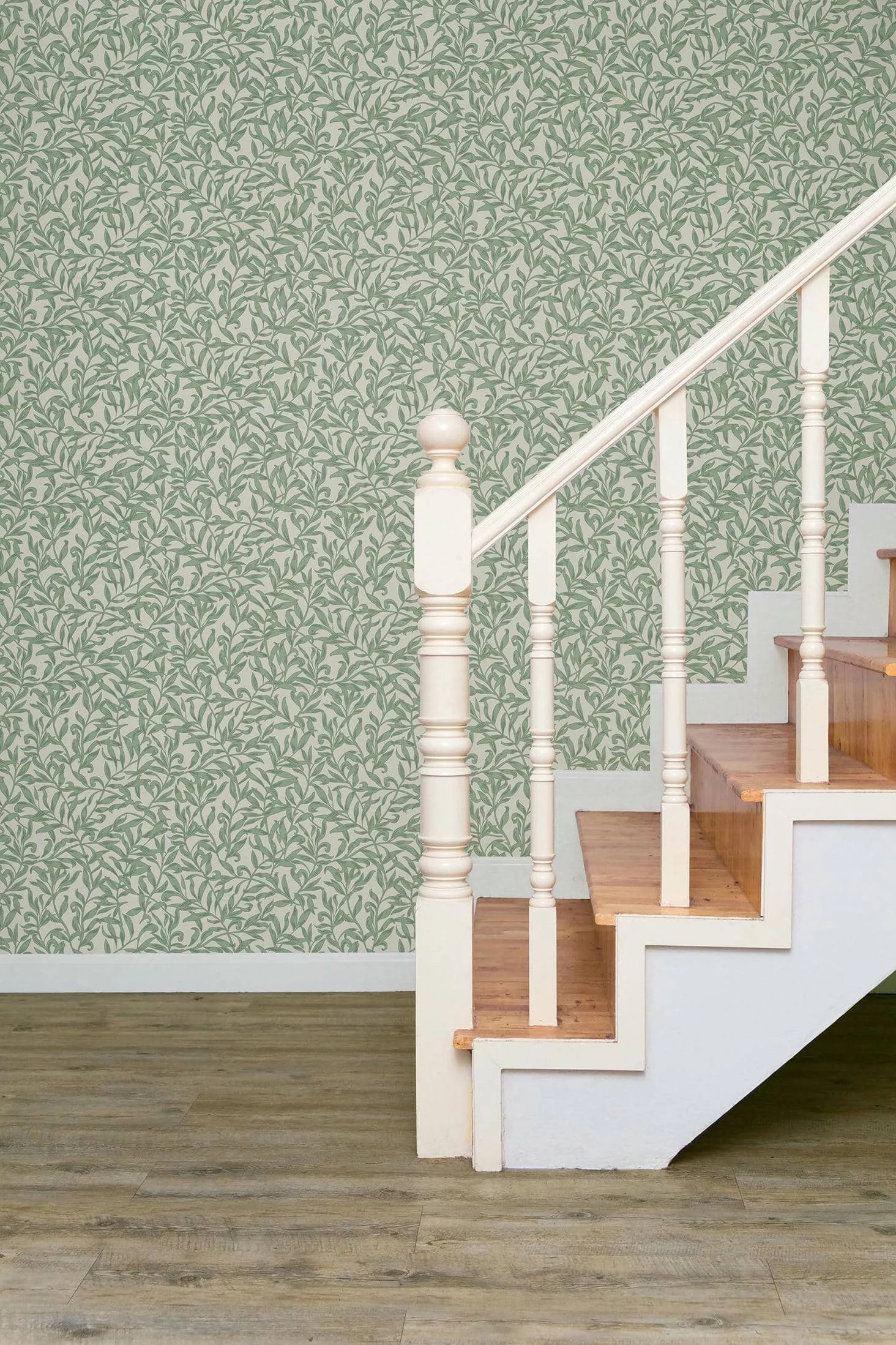 Marburg 47640 wallpaper hallway feature wall behind white balustrade staircase with wooden treads and wood plank floor, leafy pattern for a calm feel.
