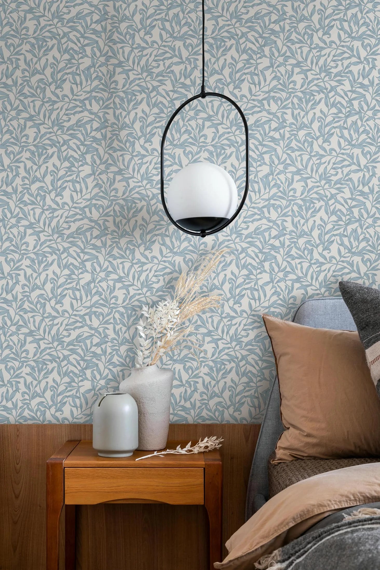 Marburg 47642 wallpaper serene bedroom feature wall behind a wooden side table with ceramic vases and dried stems, a pendant light, and an upholstered bed with cushions.